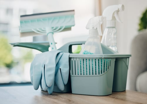 Cleaning caddy with spray bottles and gloves on a table in a bright living room
